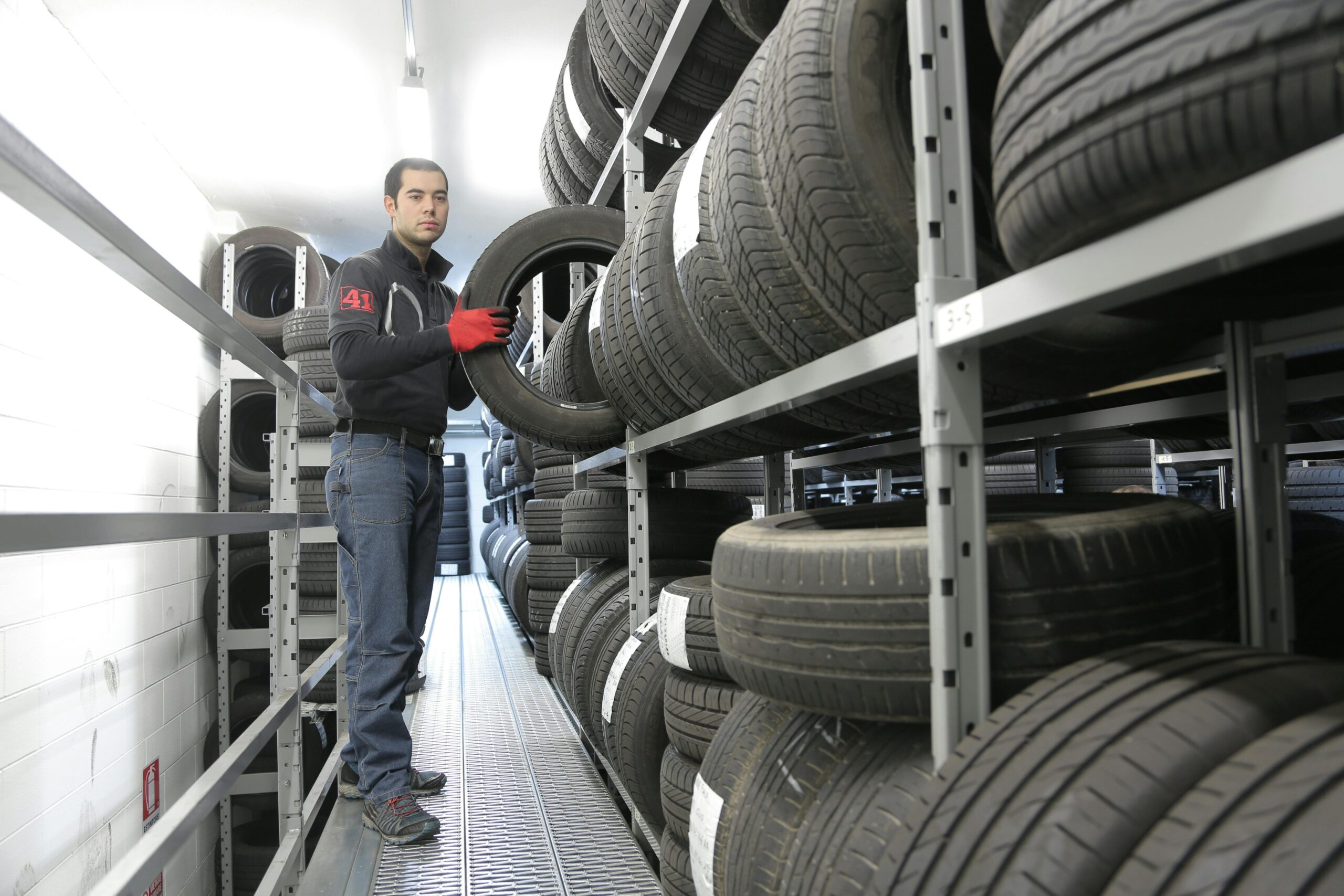 Startsida Mechanic places a tire on a rack in an indoor warehouse storage facility.